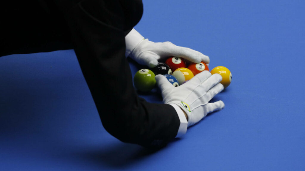 Referee with white gloves arranging billiard balls on blue table showing precision and focus Wallpaper