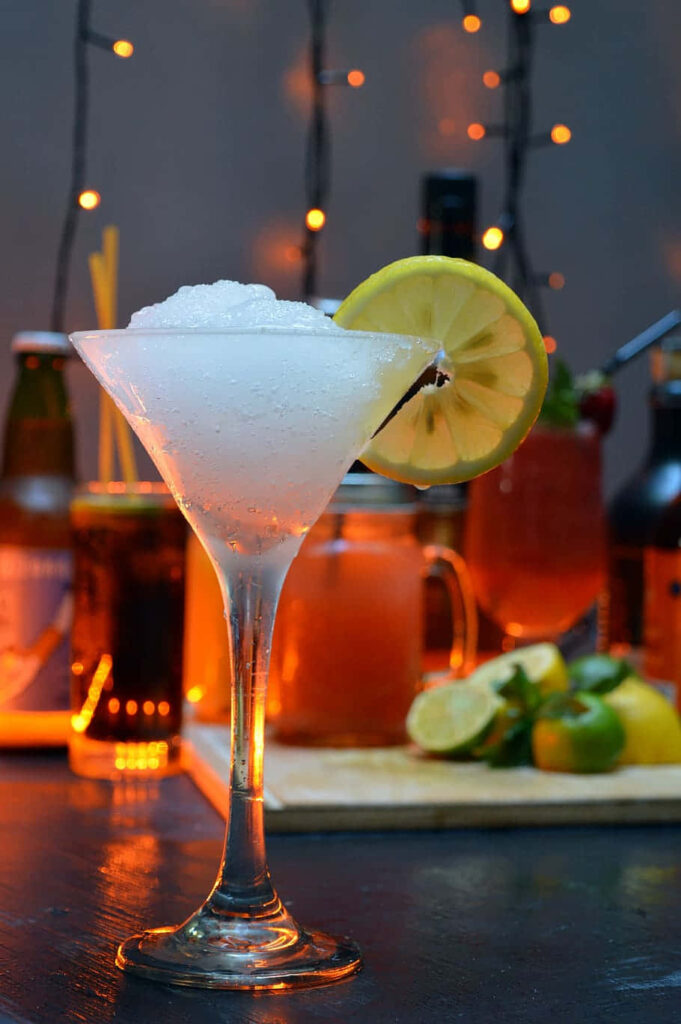 Refreshing Absinthe Frappe cocktail in martini glass with crushed ice lemon slice festive bar lights Wallpaper