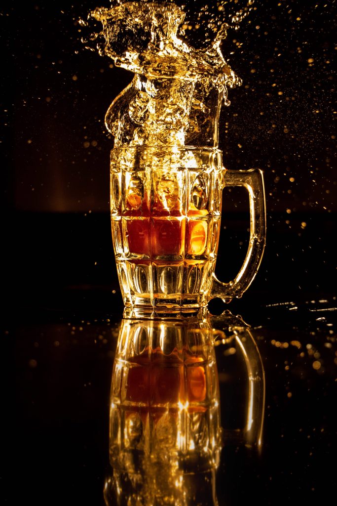 Amber beer splash in dimpled glass mug with golden light on dark reflective background wallpaper