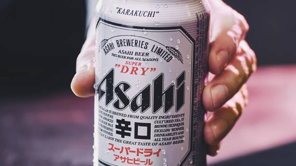 Condensation-covered Asahi Super Dry beer can held in hand with warm blurred background wallpaper