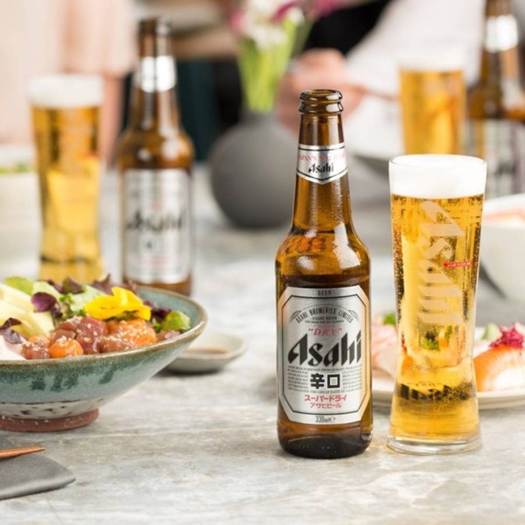 Chilled Asahi Super Dry beer bottle and glass with fresh dish on restaurant table background Wallpaper