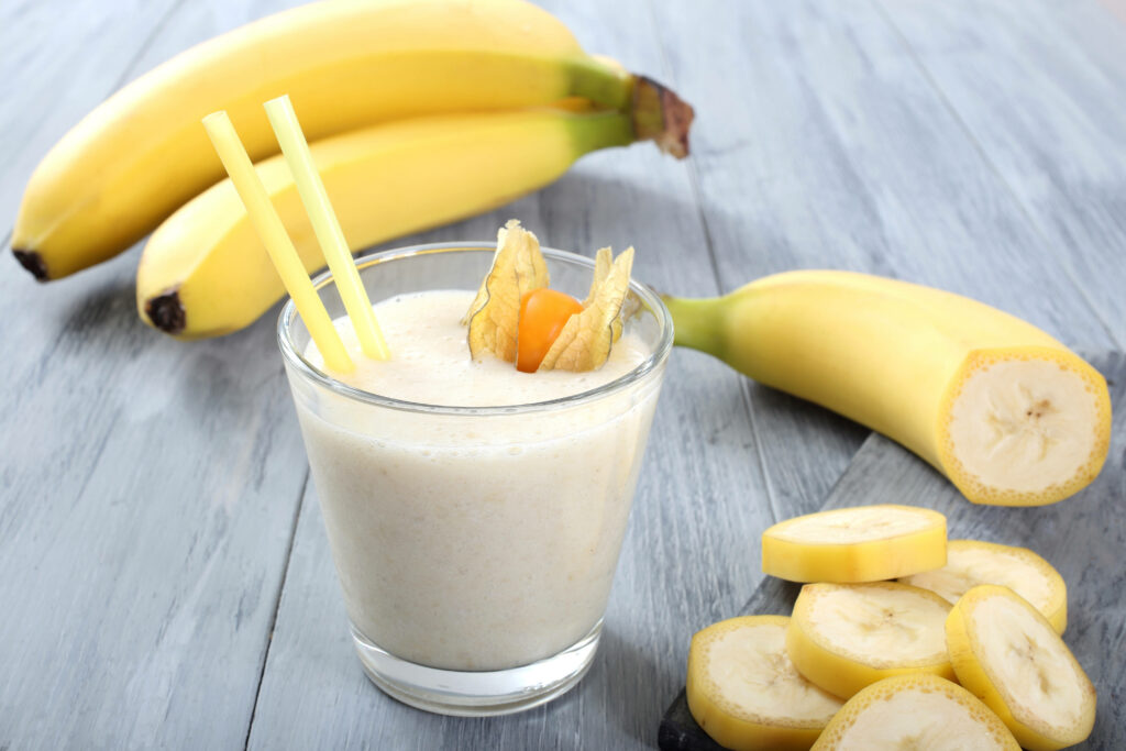 Banana milkshake with yellow straws fresh bananas and sliced banana pieces on wooden table background Wallpaper