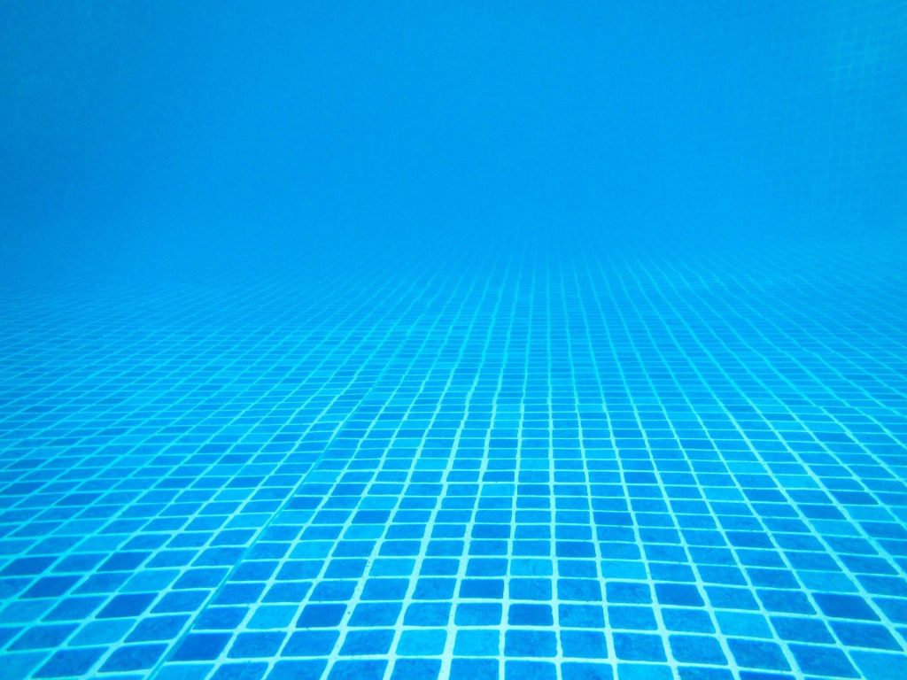 Underwater view of blue tiled swimming pool floor with clear shimmering water depth Wallpaper