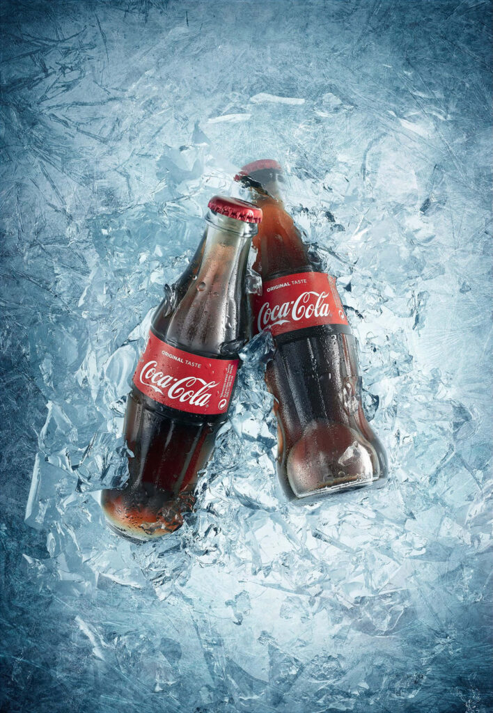 Two classic Coca-Cola glass bottles on ice showcasing refreshing iconic soft drink in vibrant colors Wallpaper