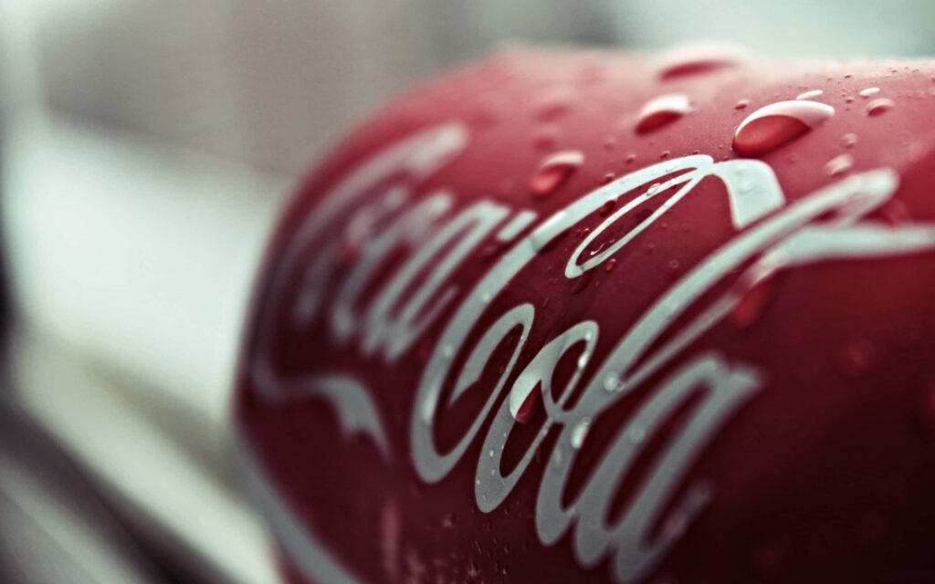 Close-up Coca Cola can with water droplets bold white logo on vibrant red background wallpaper