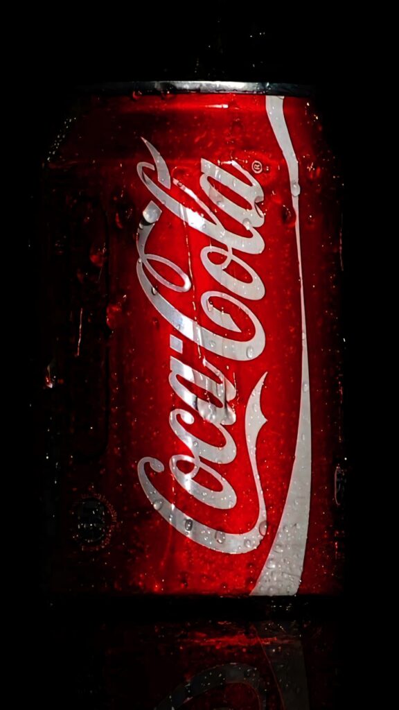 Close-up of chilled Coca-Cola can with water droplets on dark background emphasizing refreshment Wallpaper