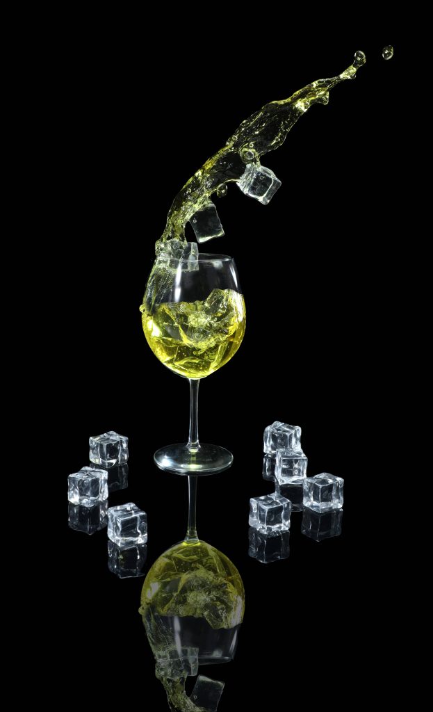 Wine glass with yellow splash and ice cubes on black reflective background studio photo wallpaper