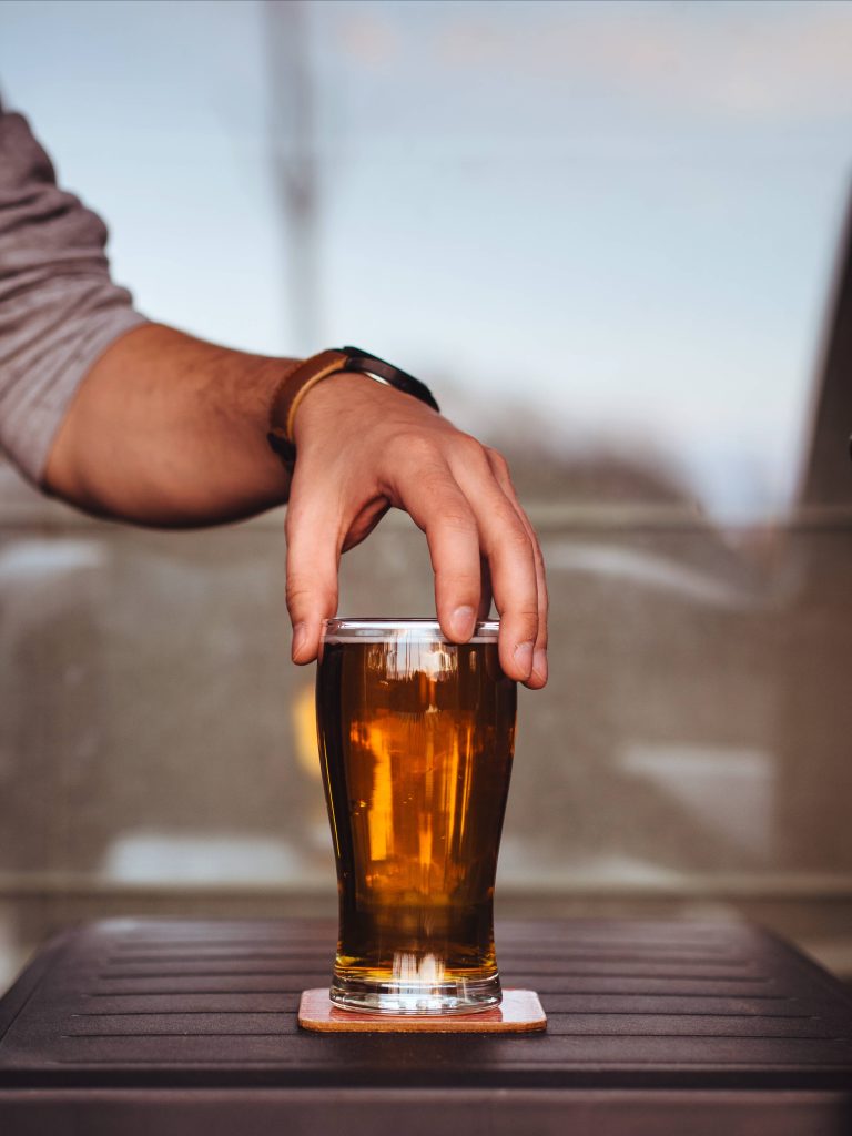 Hand with wristwatch reaching for cold golden beer on coaster in warm natural light wallpaper