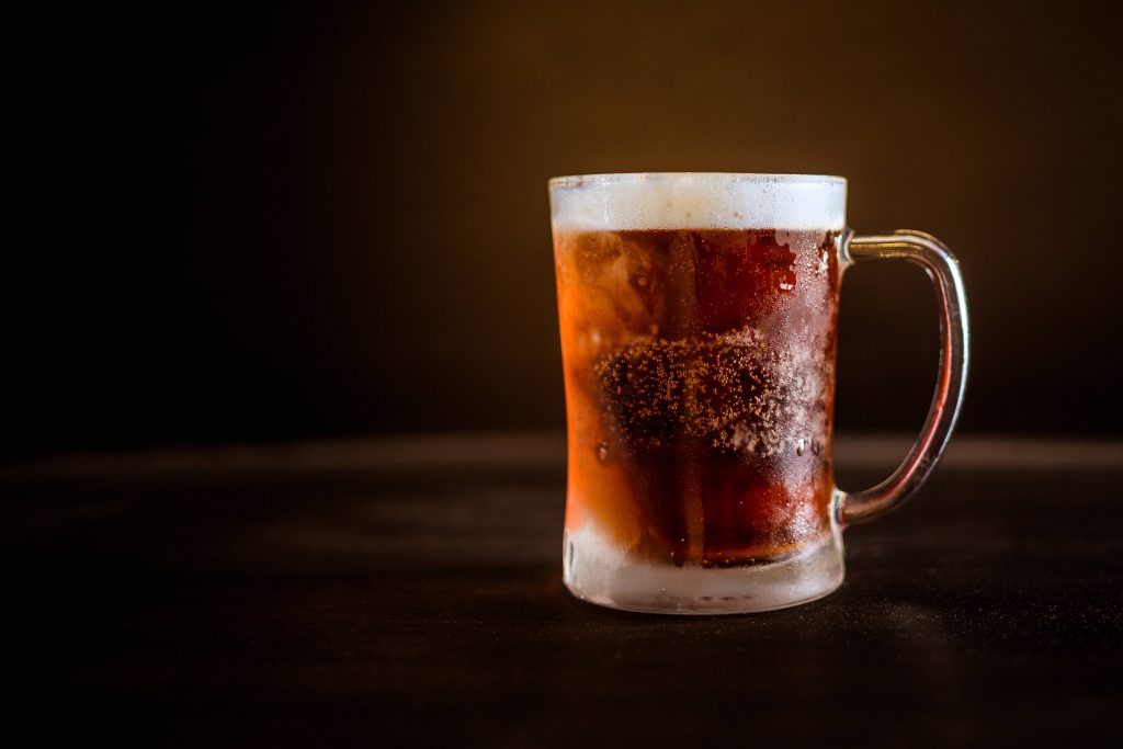 Frosty glass of amber ale beer with thick foam on dark rustic table moody lighting wallpaper