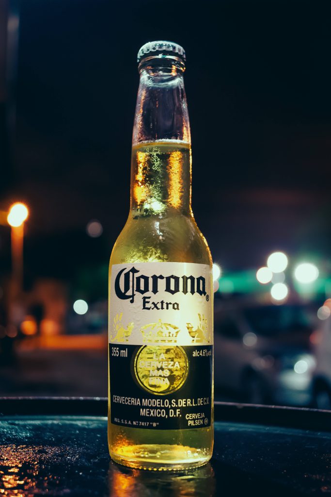 Chilled Corona Extra beer bottle with condensation against moody bokeh evening background wallpaper