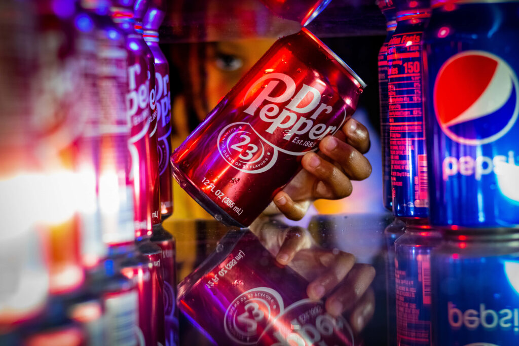 Hand reaching for chilled Dr Pepper can in fridge vibrant red blue soda wallpaper background