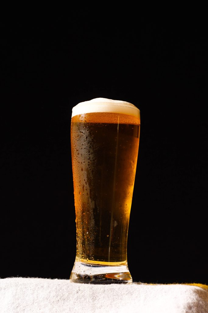 Tall glass of golden beer with frothy head and condensation on black background wallpaper