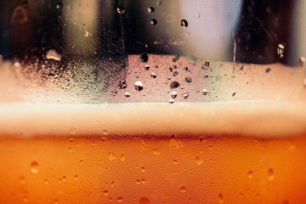Macro shot of chilled golden beer glass with frothy foam and water droplets wallpaper background