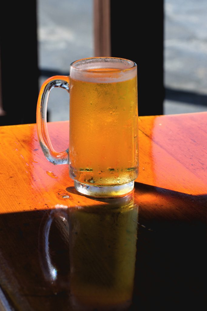 Chilled glass of golden beer on polished wooden table in warm sunlight with condensation Wallpaper
