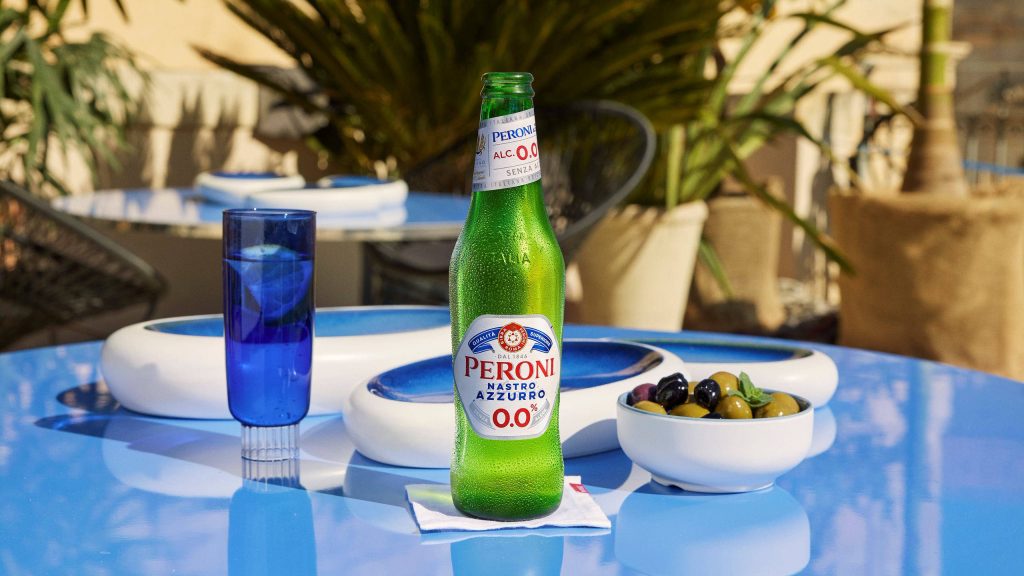 Chilled Peroni Nastro Azzurro 0.0 beer on blue table with glass and olives in Italian summer sunlight Wallpaper
