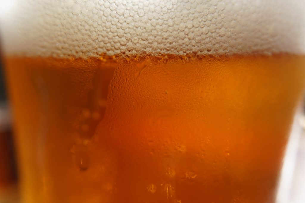Close-up of chilled golden beer with frothy foam and condensation droplets on glass surface Wallpaper