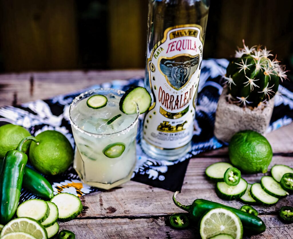 Vibrant margarita with cucumber jalapeno garnish beside Corralejo Tequila lime cactus background Wallpaper