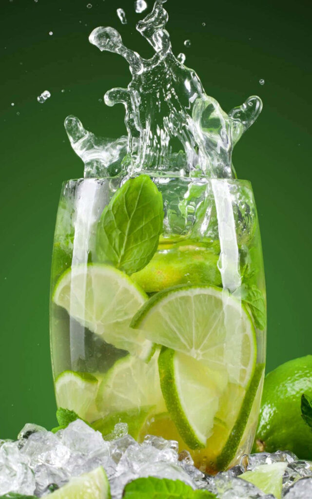 Fresh mojito cocktail with lime mint splash and ice cubes on vibrant green wallpaper background