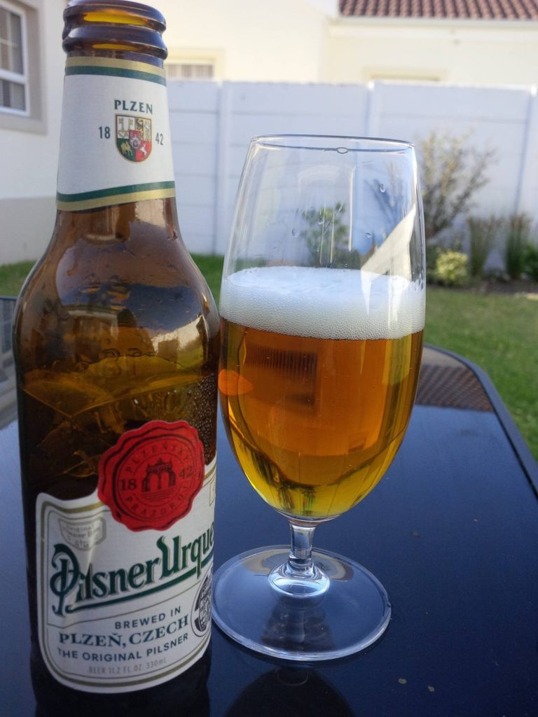 Pilsner Urquell bottle and glass of golden beer with frothy head on reflective table outdoors Wallpaper