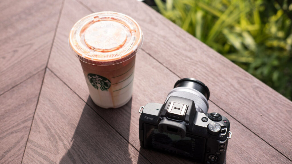 Starbucks cup beside camera on wooden table in natural light creative workspace background wallpaper