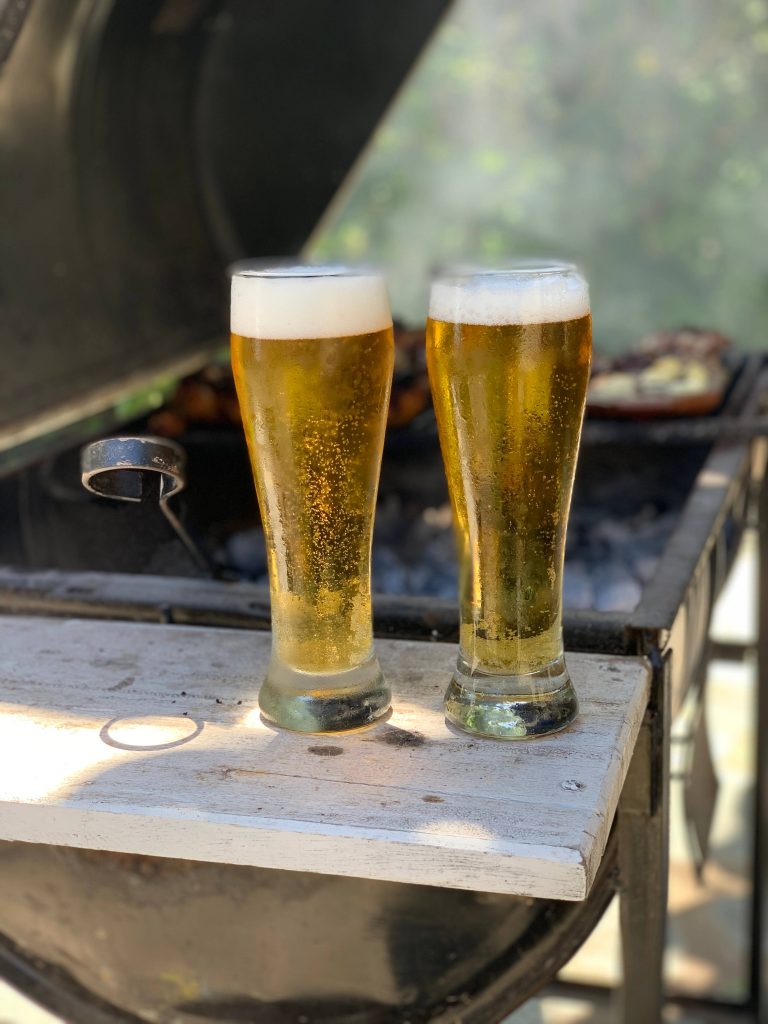 Two tall glasses of cold golden beer outdoors near barbecue grill on sunny summer day background Wallpaper