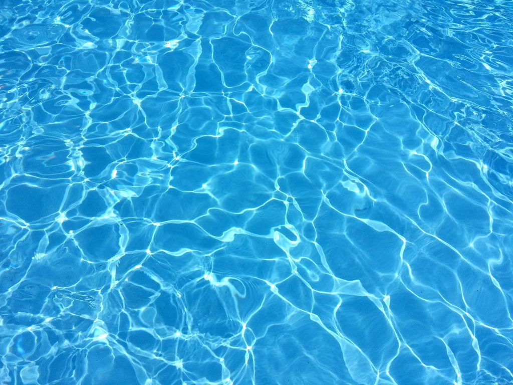 High-angle view of shimmering crystal clear swimming pool blue water with sunlight patterns Wallpaper