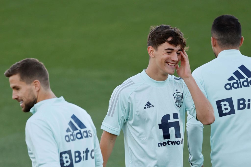 Gavi smiling in light blue Adidas Spain kit training on green blurred football pitch background Wallpaper