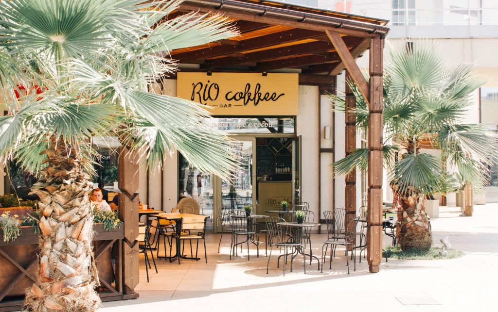 Sunlit Rio coffee shop patio with palm trees wooden decor and metal cafe seating wallpaper