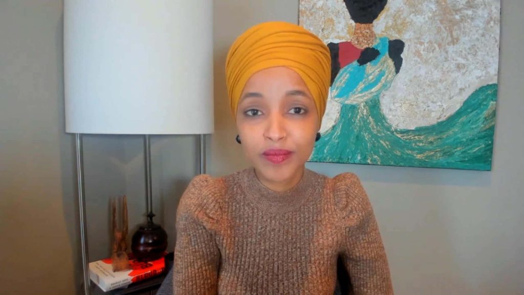 U.S. Representative Ilhan Omar in yellow headwrap and brown sweater on video call background wallpaper