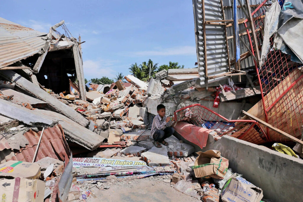 Young boy sitting amid earthquake rubble and collapsed buildings showcasing resilience and disaster Wallpaper