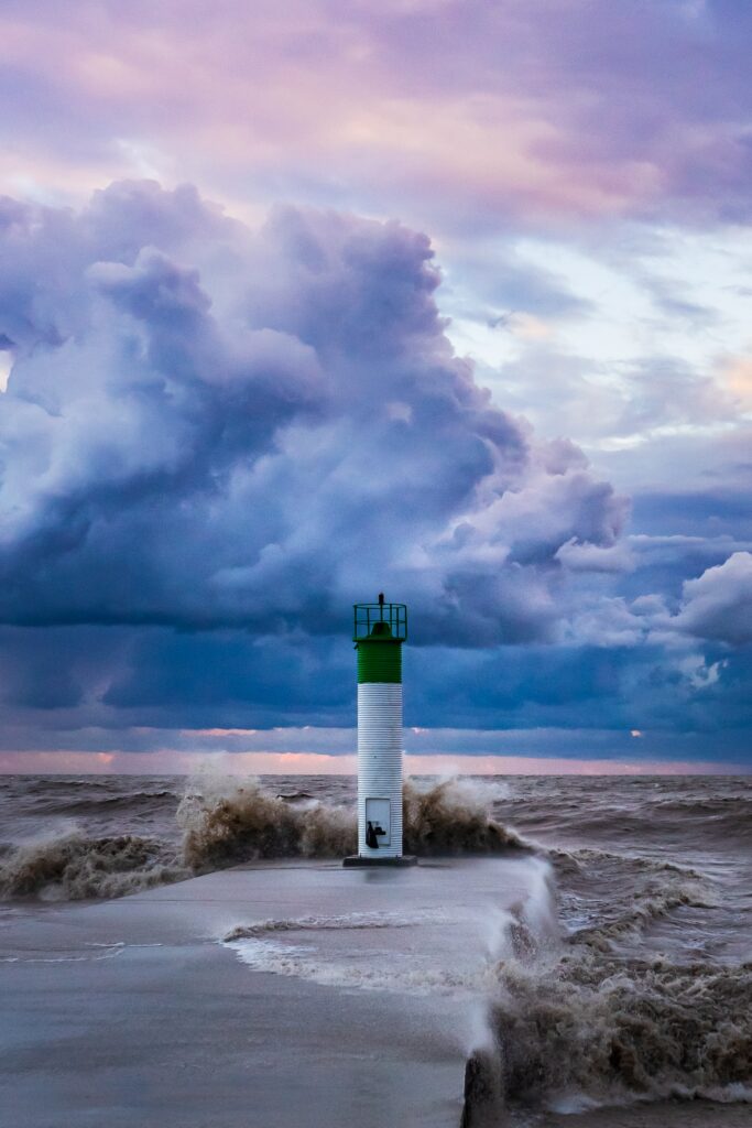 Solitary lighthouse on rocky coast with crashing surf and pastel clouds dramatic seascape wallpaper