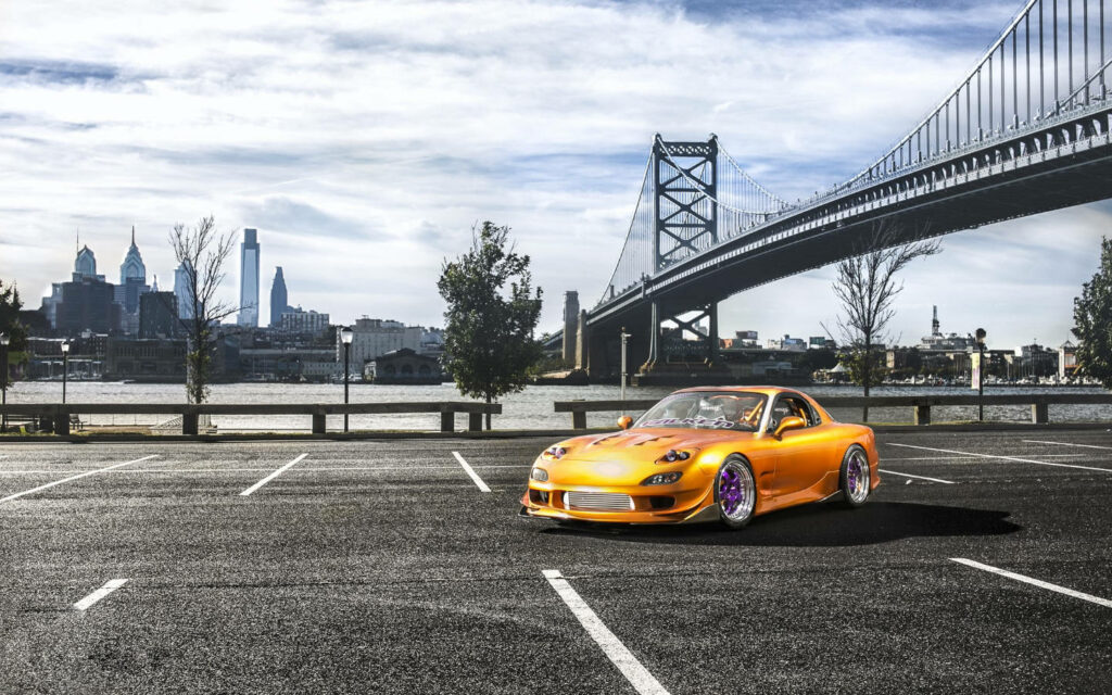 Retro Charm: A Yellow Vintage Mazda Rx-7 with Stunning Purple Wheels, Adorned by City Skyline and Waterfront, Captured in Serene Solitude Wallpaper