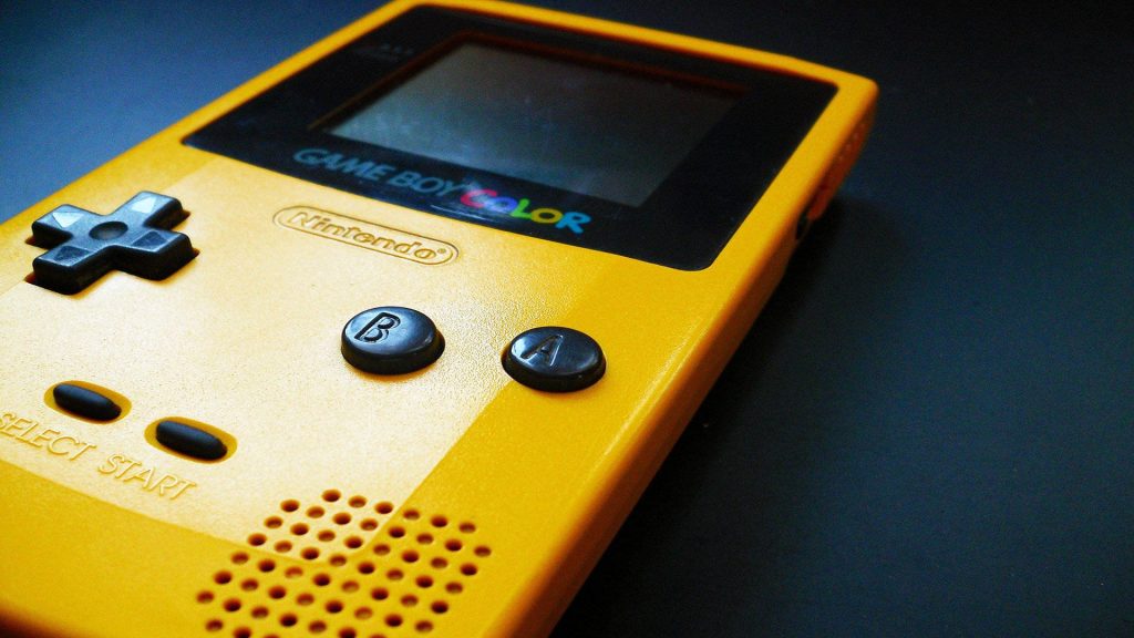 Close-up of classic yellow Nintendo Game Boy Color handheld console against dark background Wallpaper