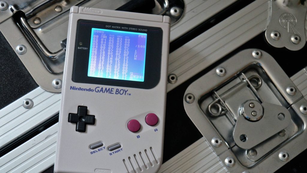 Original grey Nintendo Game Boy on metal surface with backlit chiptune music tracker interface Wallpaper