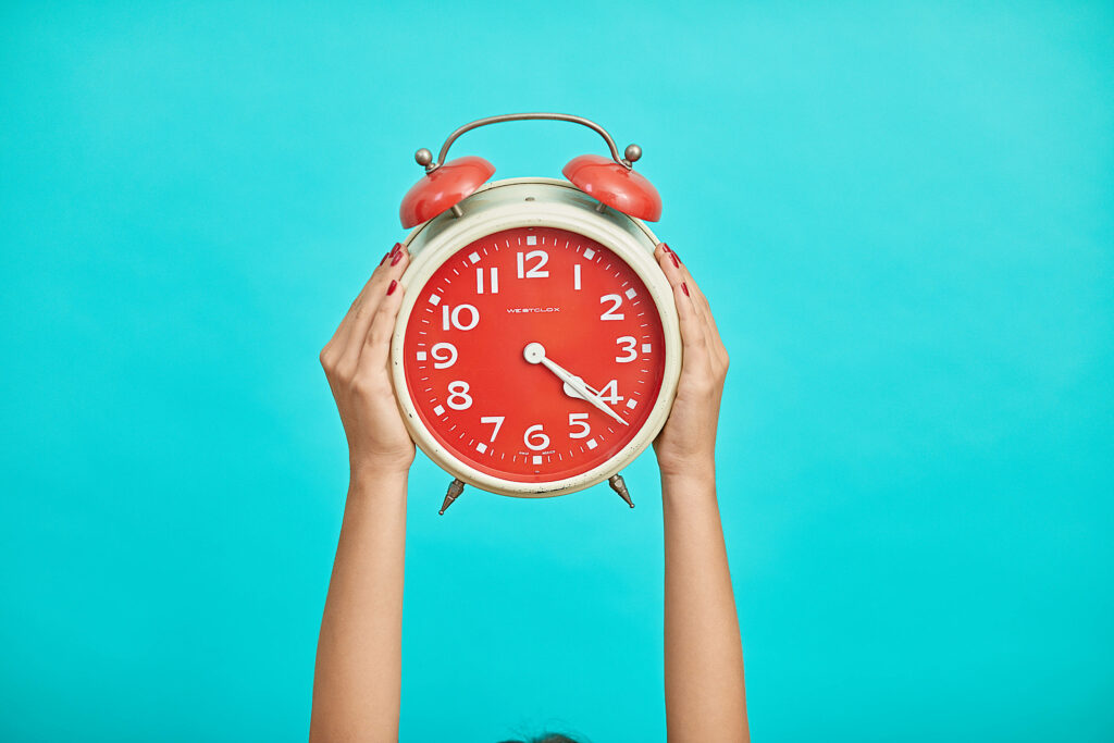 Retro red alarm clock held by hands on bright blue green background vibrant wallpaper