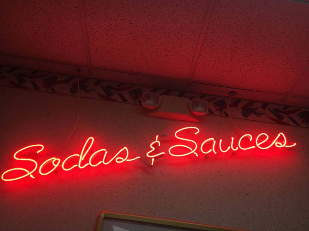 Red neon sign reading Sodas and Sauces on textured wall with retro diner ambiance wallpaper