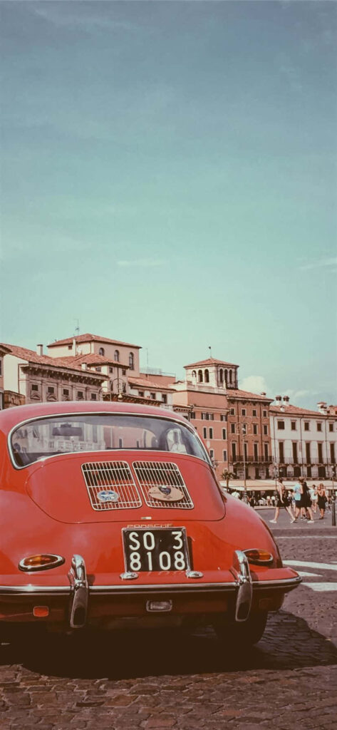 Retro iPhone wallpaper of red Porsche 356 in sunlit European square with historic buildings and blue sky