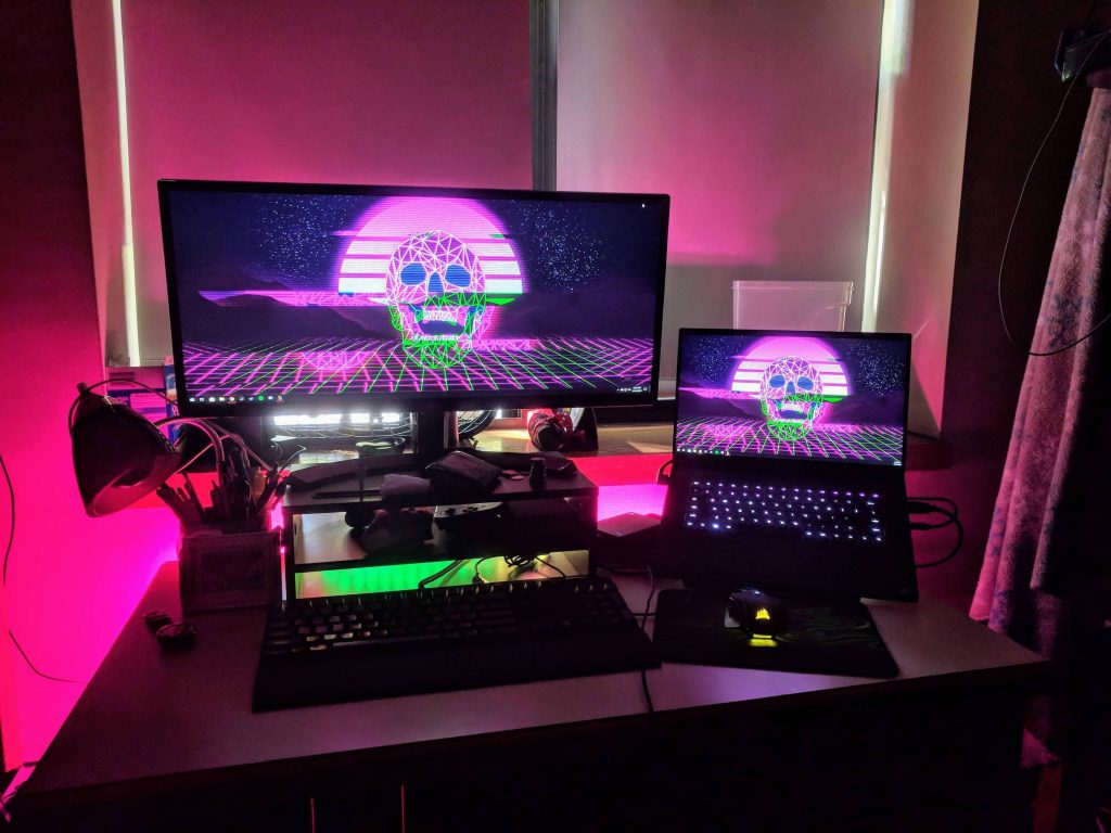 Retro-wave gaming desk setup with neon purple wireframe skull synthwave wallpaper ambiance