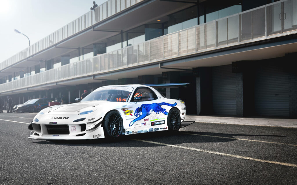 Blue Jaguar Accentuates White Mazda Rx-7's Sleek Look Against Urban Backdrop Wallpaper