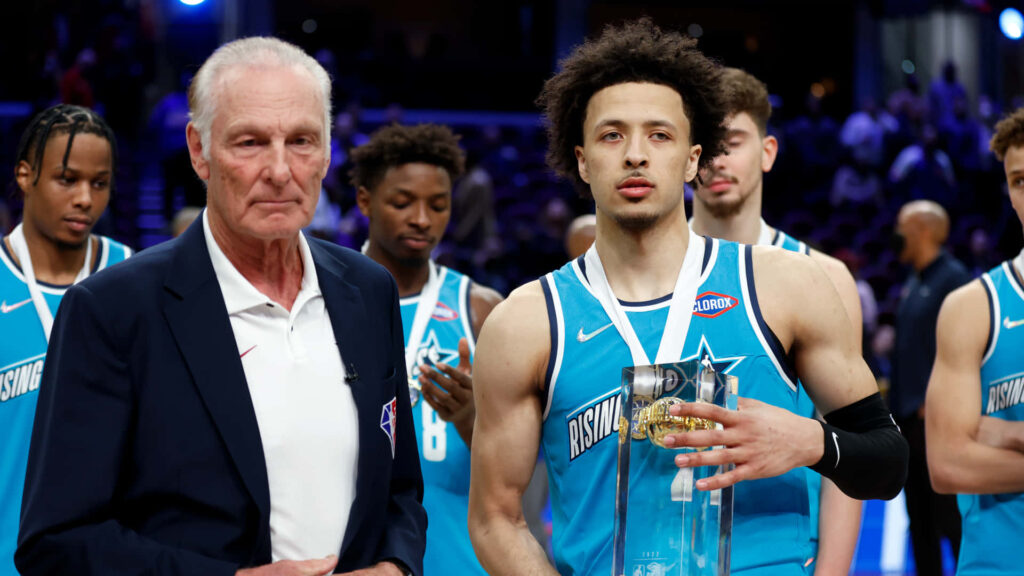 Rick Barry and Cade Cunningham celebrate with NBA Rising Stars trophy under bright arena lights Wallpaper
