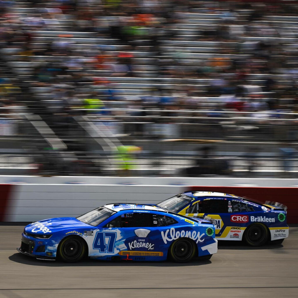 Ricky Stenhouse Jr in blue Kleenex NASCAR car overtaking rival on track with blurred fans background Wallpaper