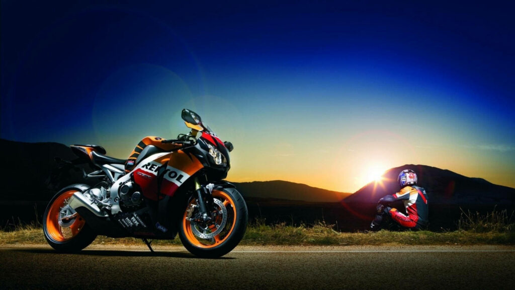 Vibrant livery racing motorcycle parked beside open road at dusk with rider in full gear - motorcycle culture background image Wallpaper