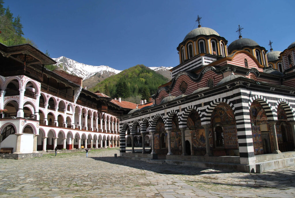 Rila Monastery courtyard with striped arches colorful domes lush mountains and blue sky wallpaper