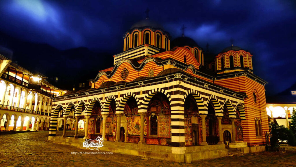 Rila Monastery Bulgaria illuminated at night with striped domes and cloudy sky wallpaper background