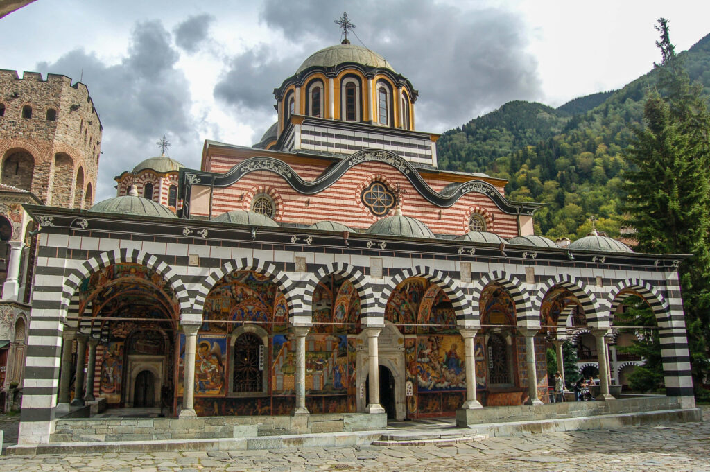 Rila Monastery veranda with intricate arches colorful frescoes and scenic mountain background wallpaper