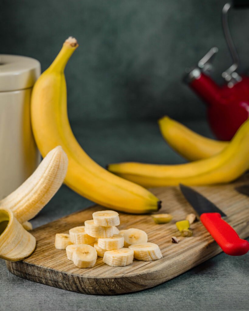 Ripe banana on rustic cutting board with blurred bananas in vibrant fresh kitchen background Wallpaper