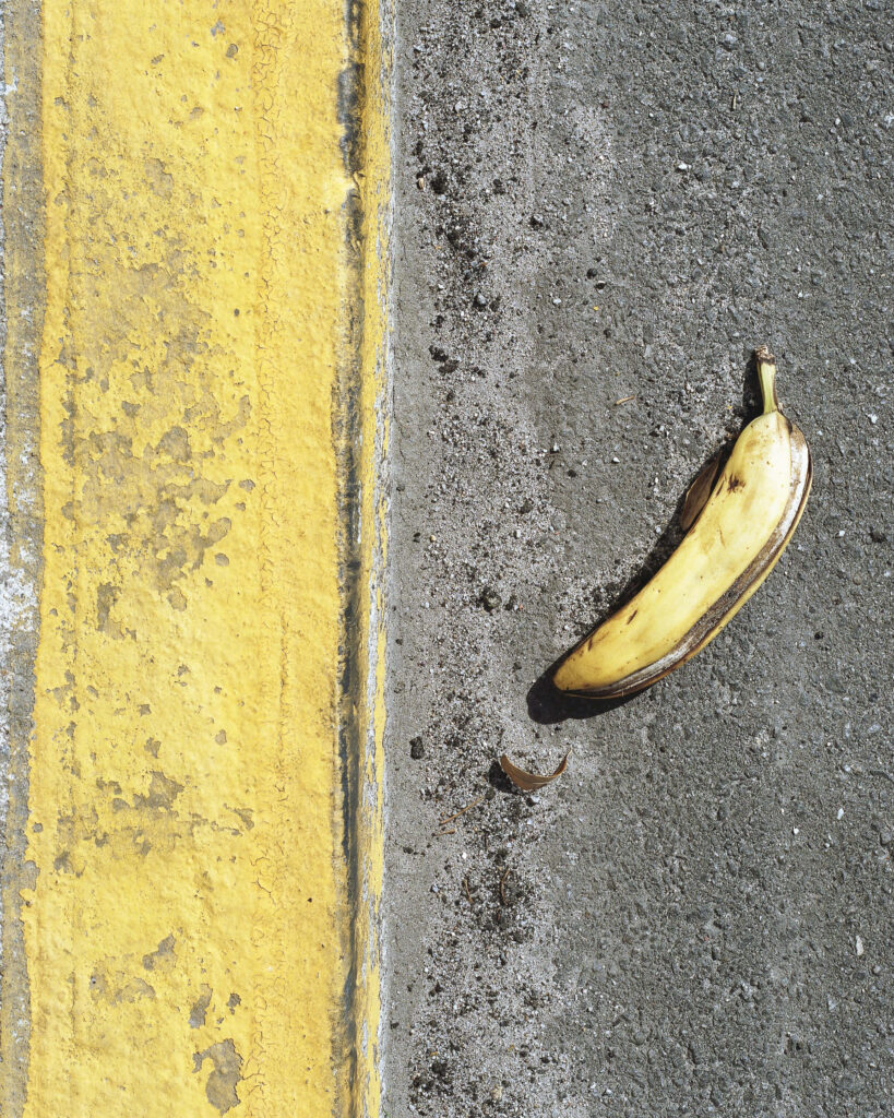 Ripe banana on rough pavement next to faded yellow street line urban contrast wallpaper