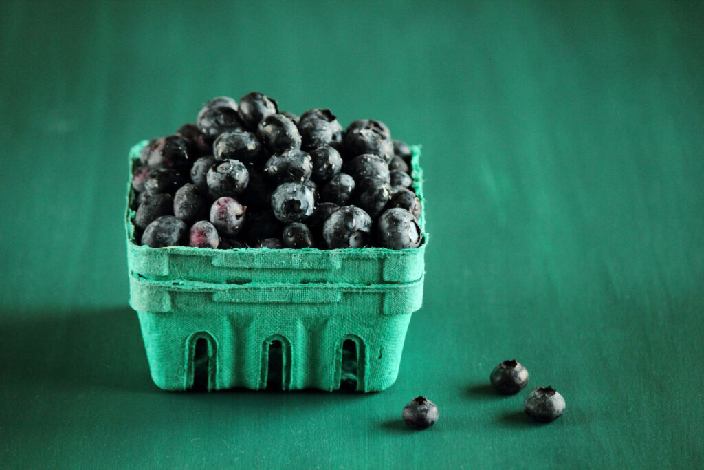 Carton of ripe fresh blueberries on vibrant green surface colorful natural wallpaper background