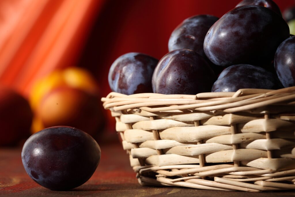 Ripe Plums in Wicker Basket: Vibrant Wallpaper Background Close-Up