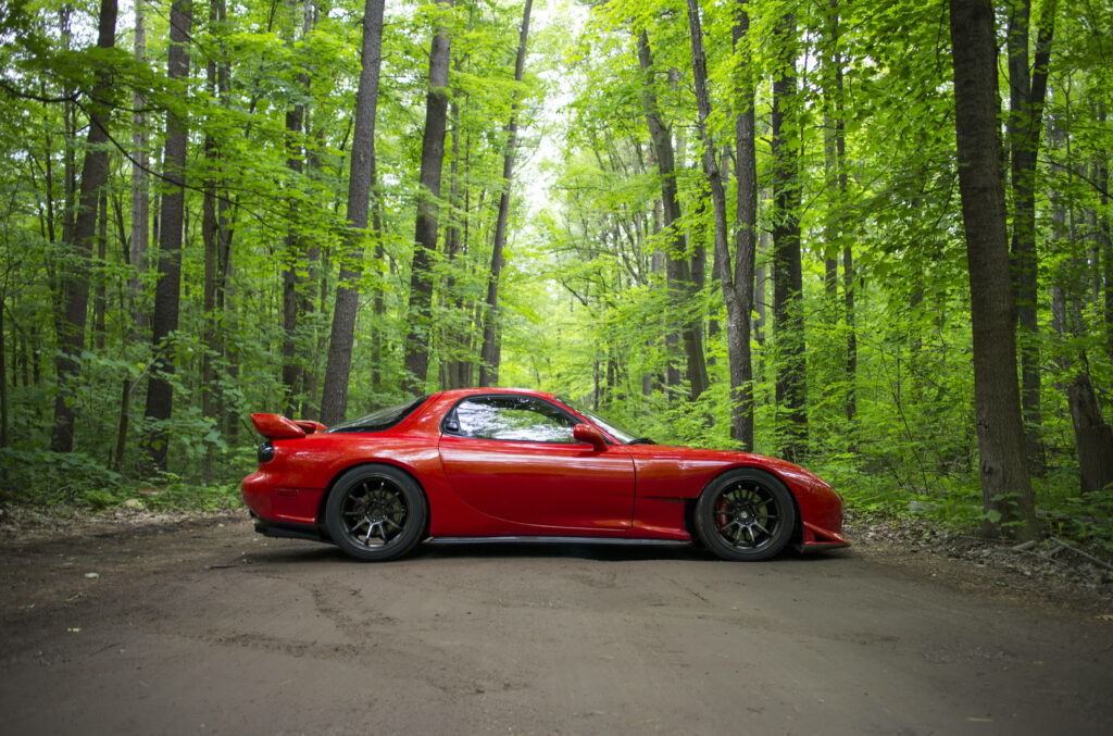 Unleashing the Power: A Captivating Red Mazda RX-7 Roams Majestic Woods, Flanked by Towering Trees and Scenic Rocks Wallpaper